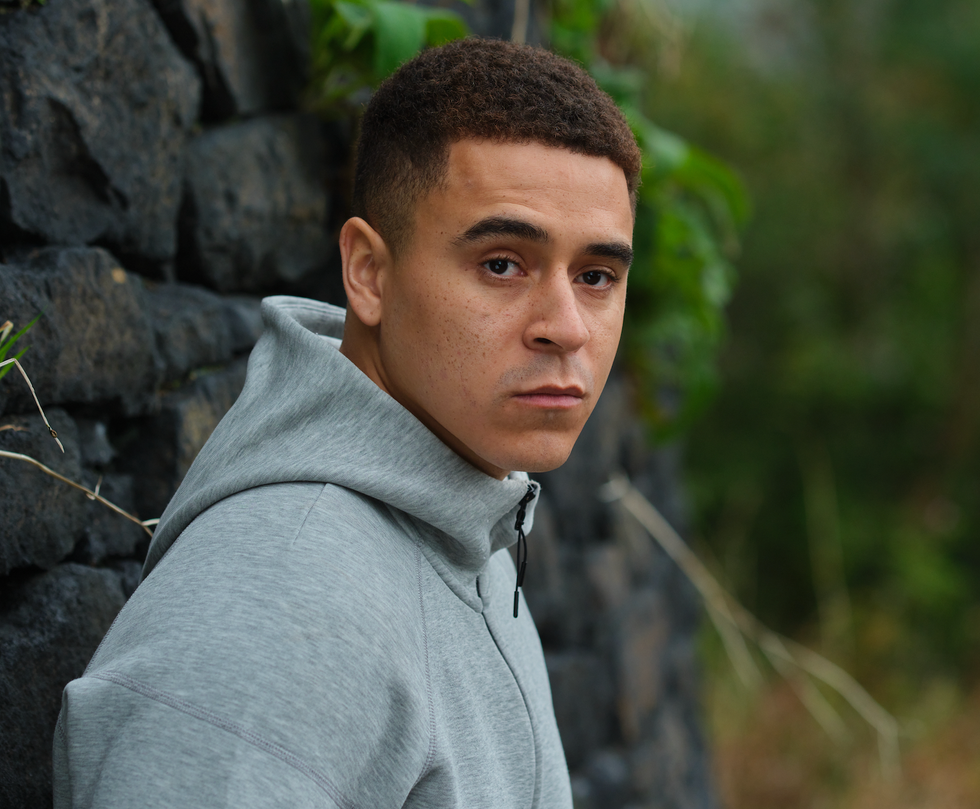 outdoor portrait with a person dressed in a gray hoodie standing near a stone wall