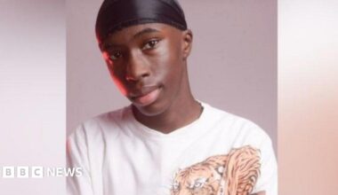 Jibrael Fehintola wearing a black cap on his head. He is looking at the camera and not really smiling. He is also wearing a white top with a tiger on the right hand side.