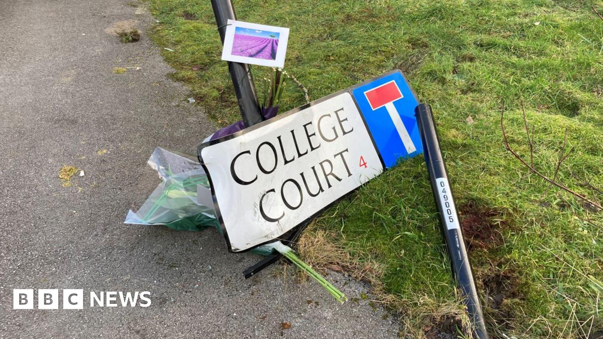 Flowers are left next to a road sign displaying "College Court", which has been knocked over.