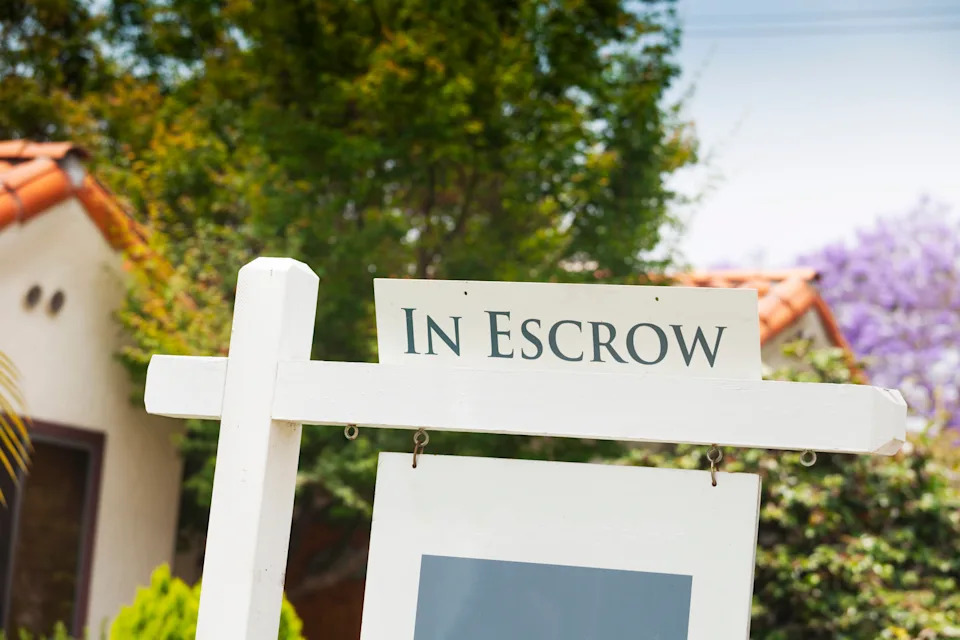 Real estate sign reading "In Escrow" outside a house, indicating a pending property sale