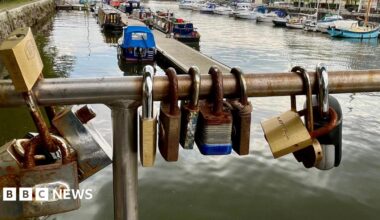 A close-in view of padlocks attached to the metalwork of Pero's Bridge in the centre of Bristol. Behind the waterways of the floating harbour are visible along with some houseboats