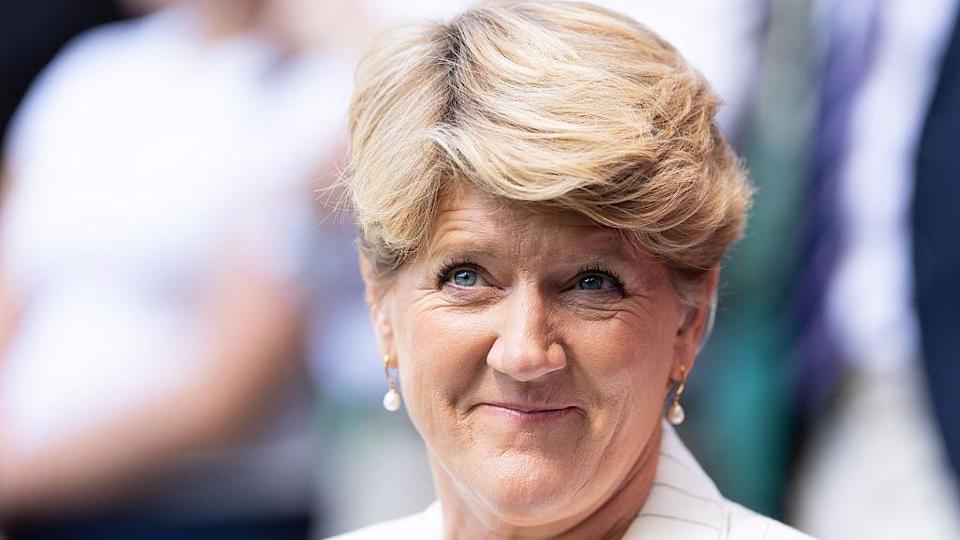 A woman with short blonde hair wearing a white jacket and gold pearl-drop earrings. She is looking off to the side and smiling. It is a headshot. 