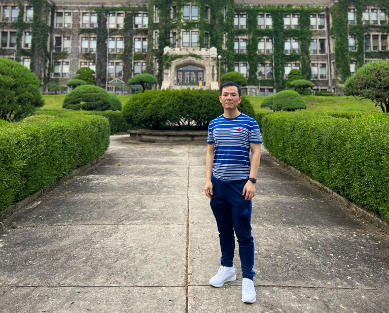 Zhicheng Lin standing on a path outside an ivy clad university building.