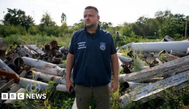 Dymtro Chubenko stands in front of a pile of Russian missile and drone parts