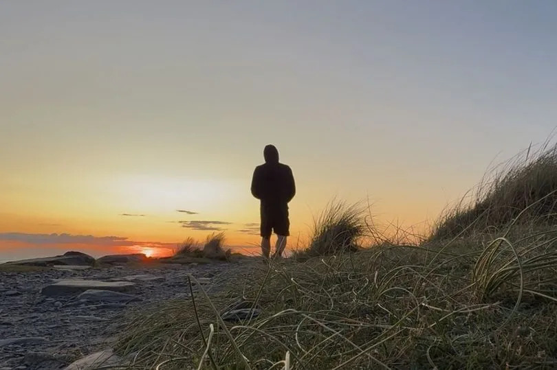 A silhouette of a man  looking into the sunset as the sky turns orange
