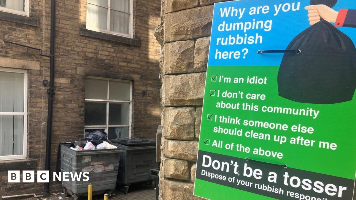 The entrance to a Bradford passageway with several large bins in it and a large green sign urging people not to dump rubbish