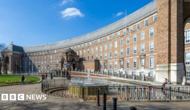 Bristol City Council City Hall. It is a wide, brown brick building with lots of windows. There is a black metal railing in front of the building and a fountain on one side.