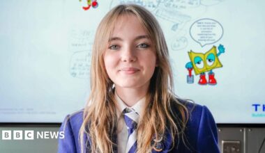 A schoolgirl, wearing blue school uniform, in front a white board detailing her heated blanket idea