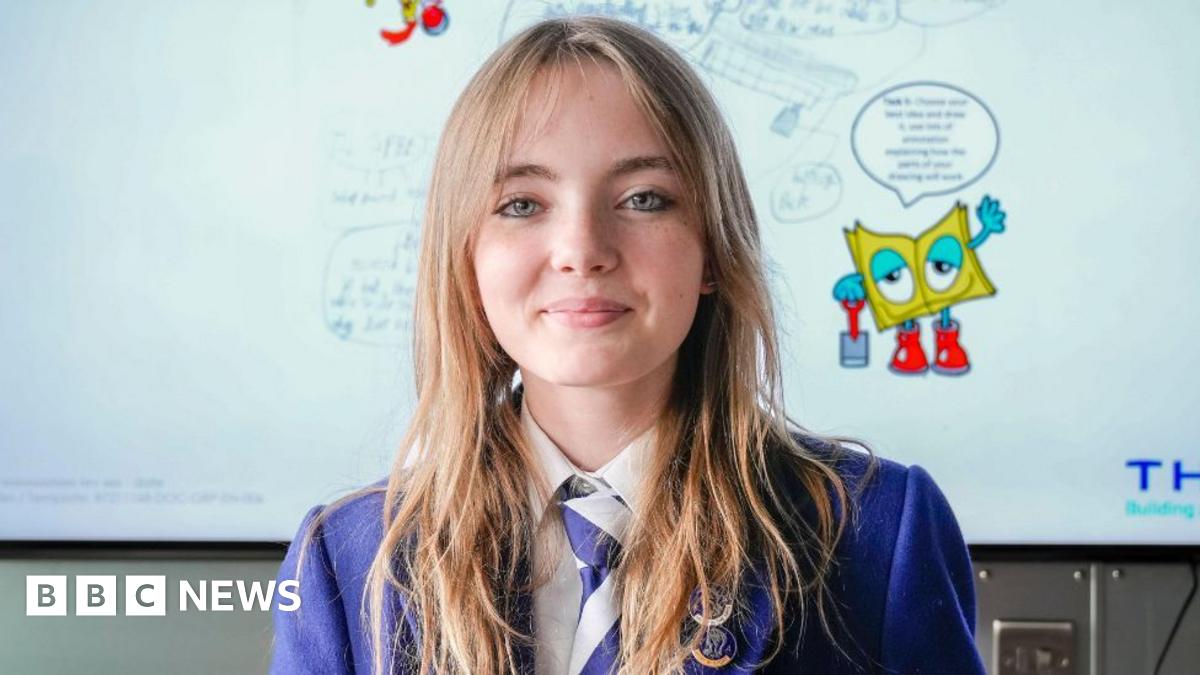 A schoolgirl, wearing blue school uniform, in front a white board detailing her heated blanket idea