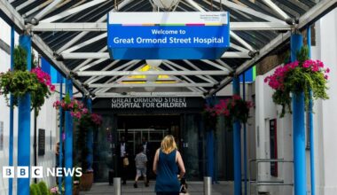 A woman walks under a blue and white sign for Great Ormond Street Hospital in its entrance.