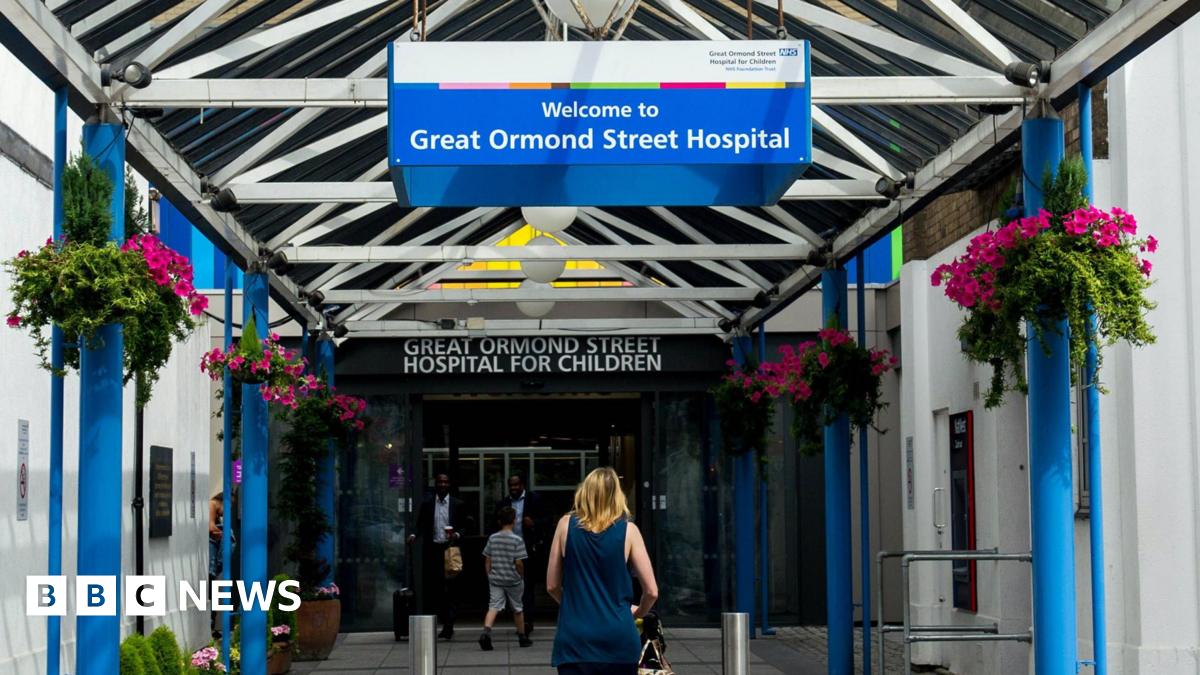 A woman walks under a blue and white sign for Great Ormond Street Hospital in its entrance.