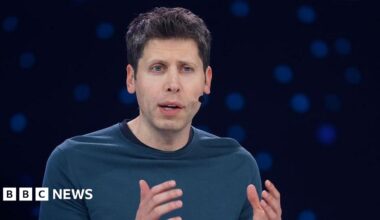Sam Altman hearing a headset microphone on stage at an event