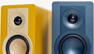 Two modern bookshelf speakers, one yellow with a beige front panel and one dark blue, each featuring a circular tweeter with radial lines and a larger woofer below.