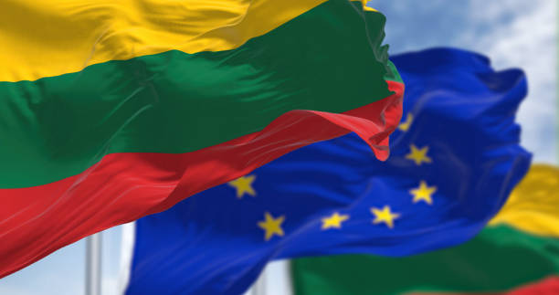 The Lithuanian flag waves in front of European Union flags against a blue sky.