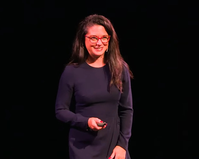 Woman wearing glasses and a dark dress speaking onstage about the doctor reveals 11 push-ups challenge for women.