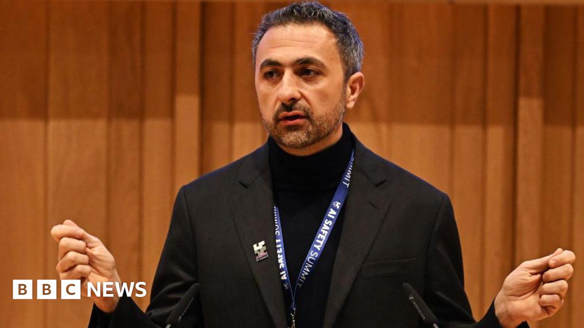 Suleyman dressed all in black, with an AI safety summit lanyard round his next, addresses the audience.
