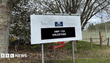 A sign outside a prison complex which reads "HM Prison Service: HMP/YOI Erlestoke". There are trees and grass behind it.
