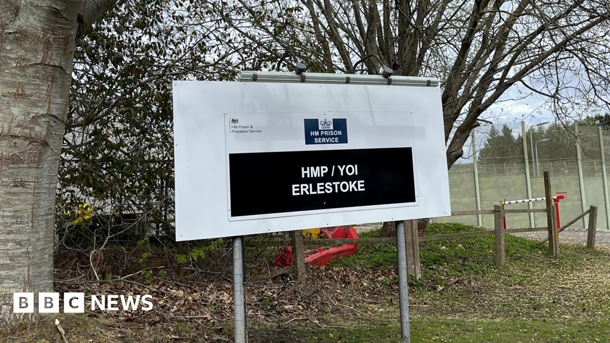 A sign outside a prison complex which reads "HM Prison Service: HMP/YOI Erlestoke". There are trees and grass behind it.