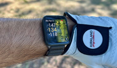 The Garmin Venu X1 on a wrist next to a golf glove, showing the yardage for the hole with fairway rough in the background.