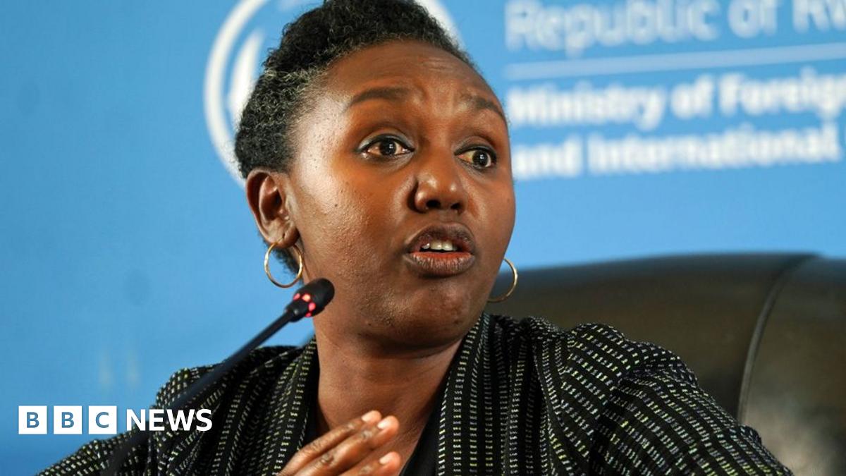 Rwanda government spokesperson Yolande Makole sits on a black chair before a microphone. She is wearing a white dotted black blazer.