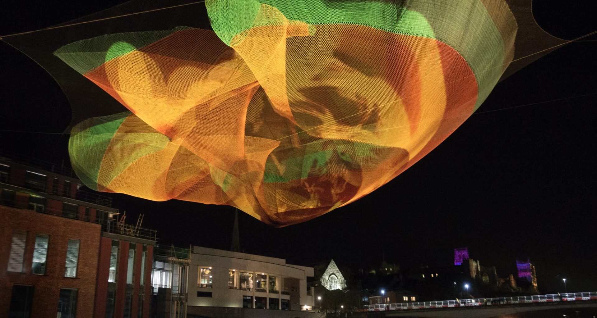 an orange and green Janet Echelman installation suspended in the air