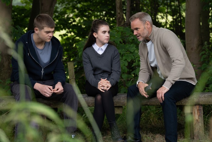 Ray sitting next to nervous April with Dylan beside her in Emmerdale