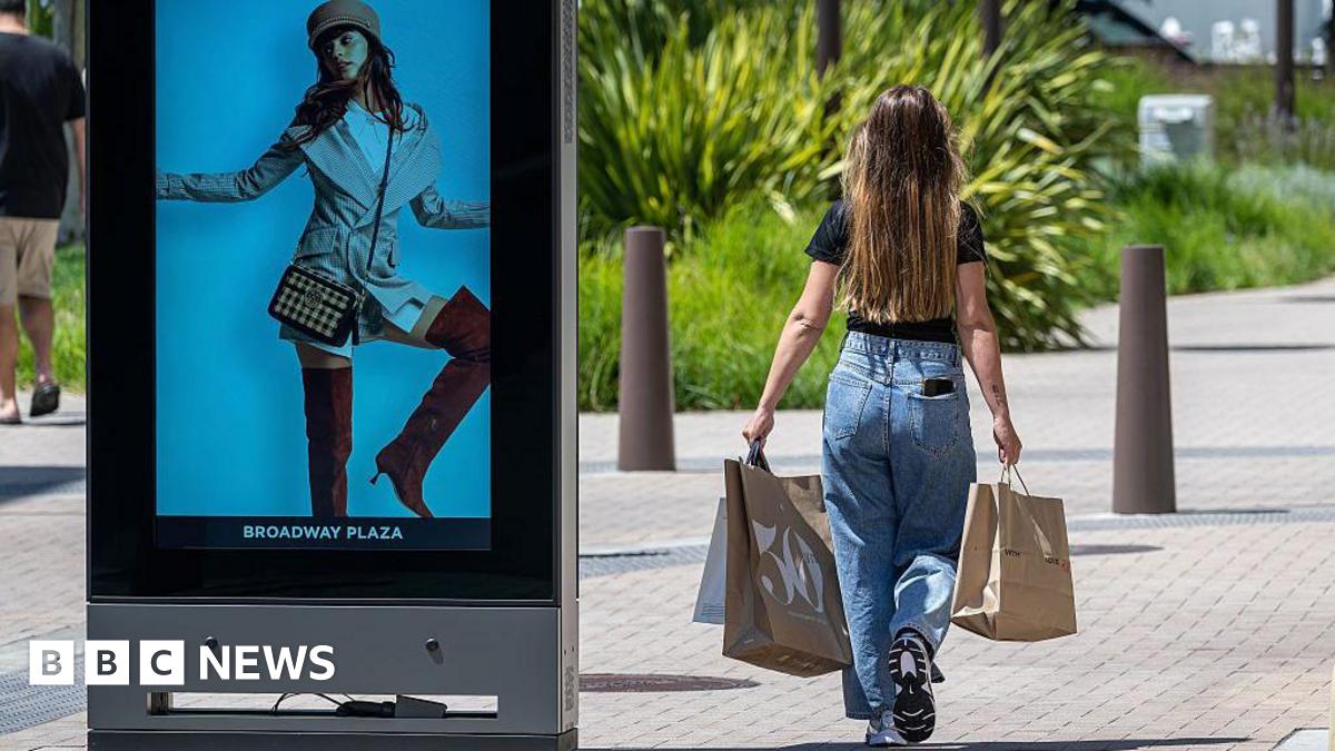 A female shopper with long brown hair at the Broadway Plaza Shopping Center in Walnut Creek, California, walking on the sidewalk carrying shopping bags