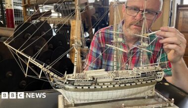 A man cleans a model ship made of ivory using a tiny paint brush