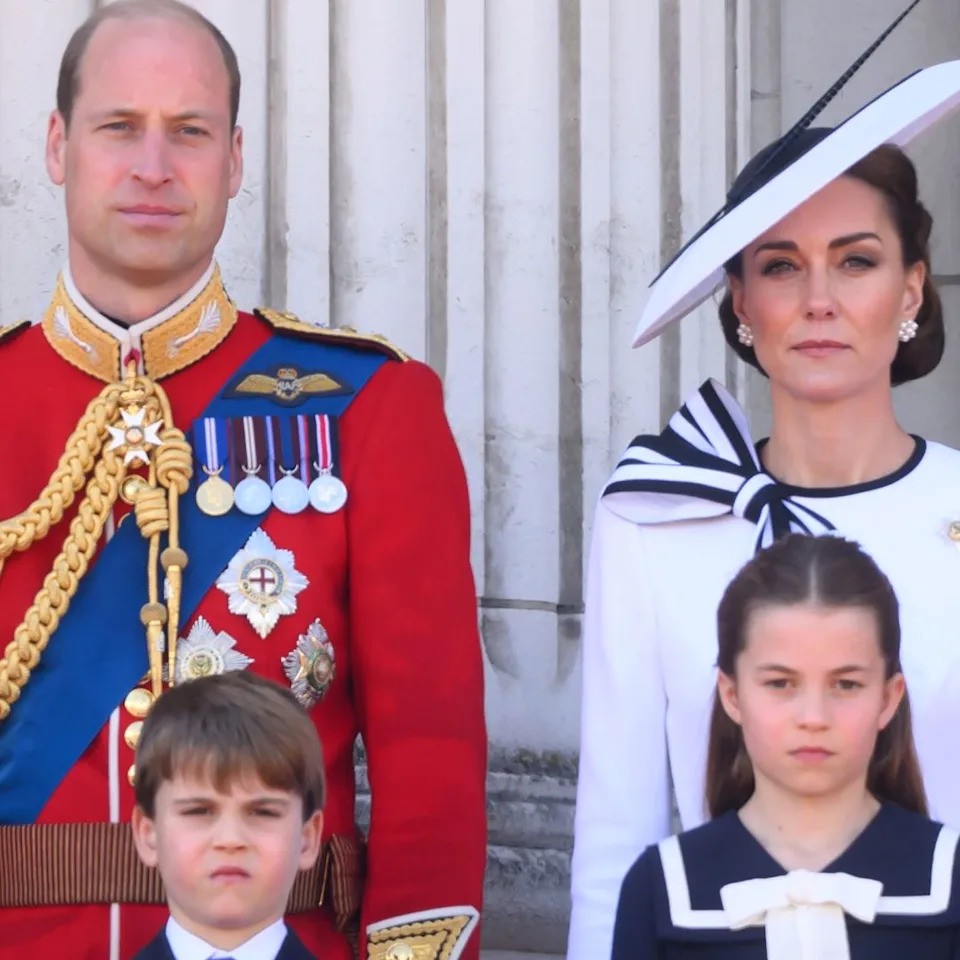  Prince William wears red military uniform and Kate Middleton wears a white dress with navy detailing, as they stand on the Buckingham Palace with their three kids, Prince George, Prince Louis, and Princess Charlotte. 