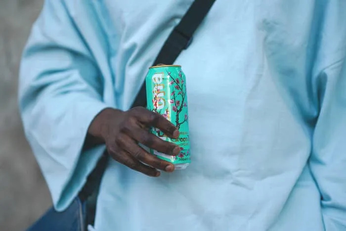 Person in a loose shirt holding a can of Arizona Green Tea with Cherry Blossom design