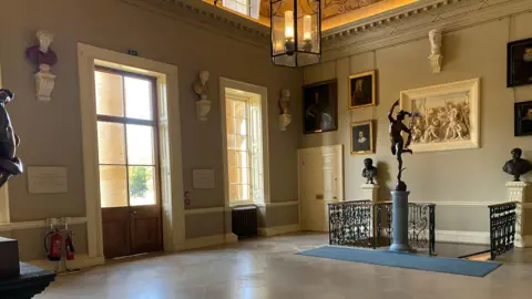 Stowe House Preservation Trust A grand hall with paintings and busts on the walls and a sculpture in the middle.