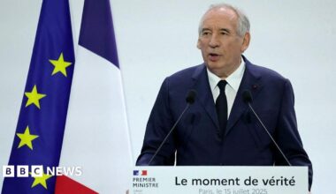 Francois Bayrou stands in front of a lectern reading "The moment of truth". Behind him are a French and an EU flag