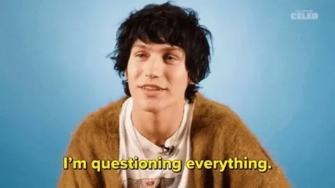 A person with shaggy hair, wearing a t-shirt and cardigan. Text reads: "I'm questioning everything."