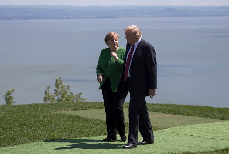 A man and a woman walk on grass while talking.