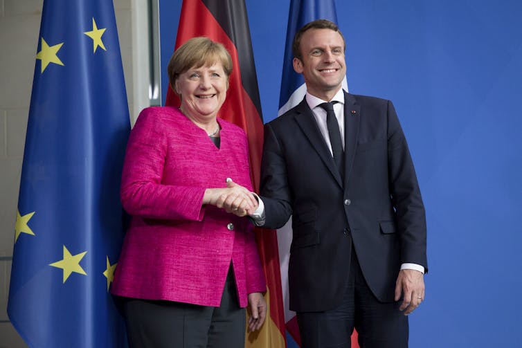 A woman in pink and a man in a suit shake hands.