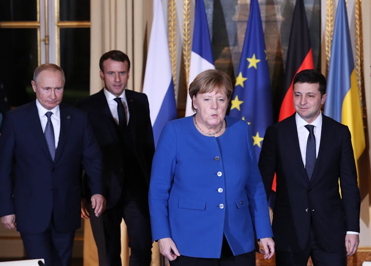 Three men in suits and a woman. in a blue top walk toward the camera.