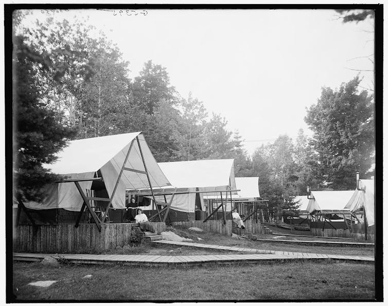 People sit outside tents surrounded by forest.