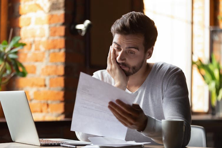 A young man looks dejectedly at a bill