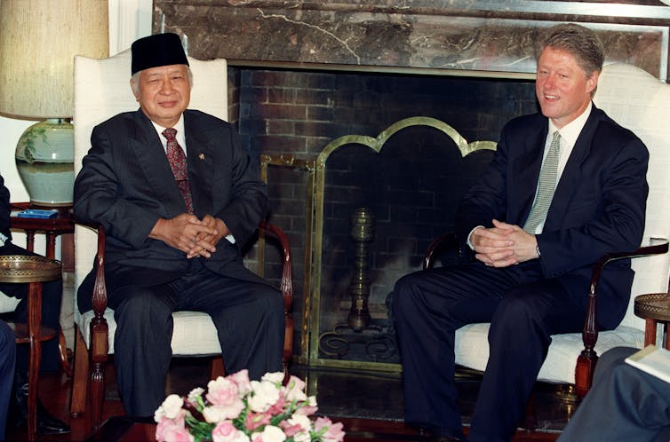 Two men sitting in high-backed chairs in front of a fireplace.