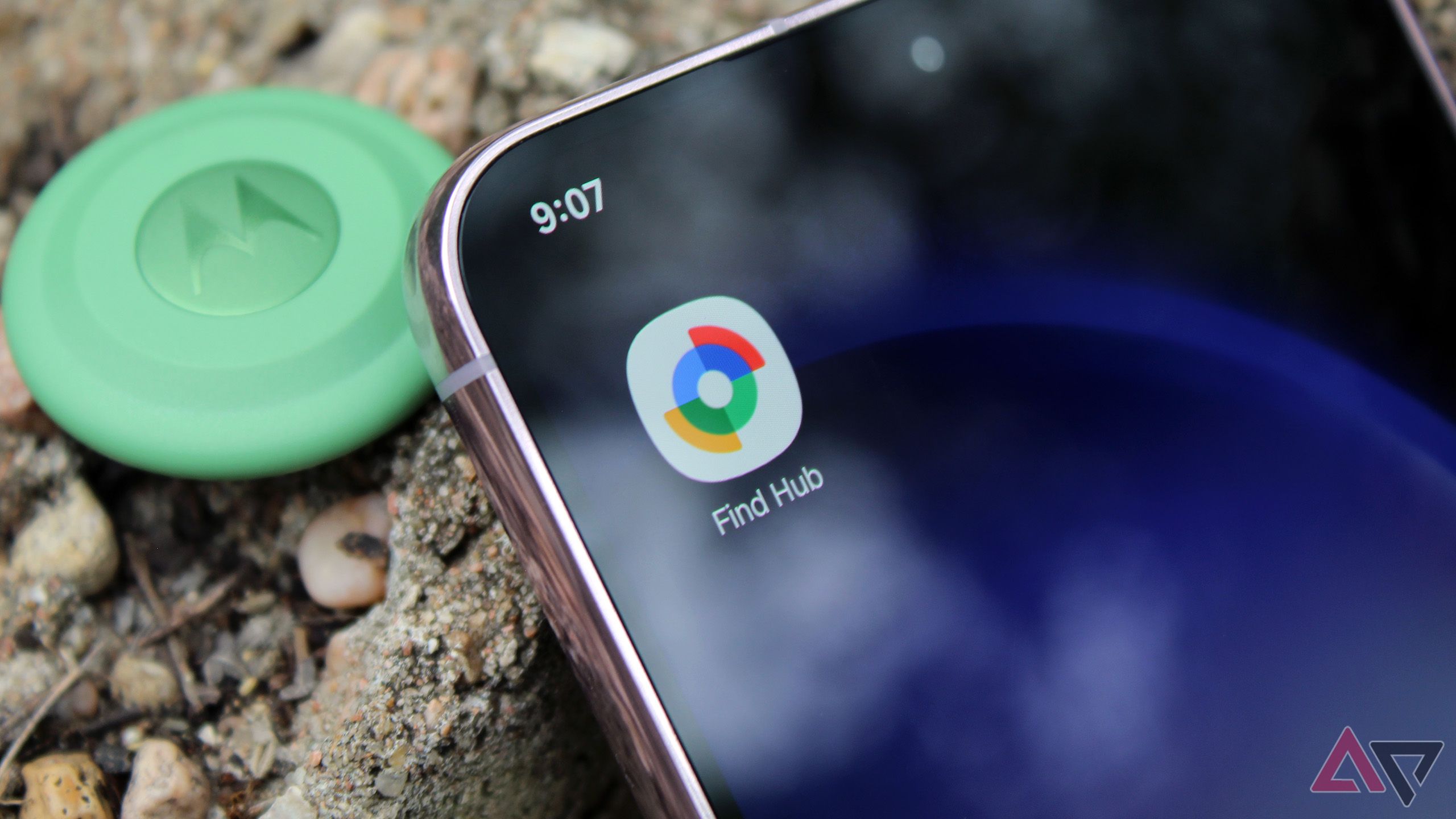 The Find Hub app on a phone's home screen while the device is next to a Moto Tag sitting on a rock.