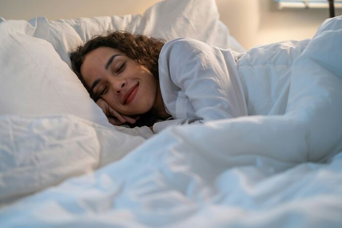 A woman peacefully sleeping under white blankets, illustrating cool facts about the human body and its fascinating functions.