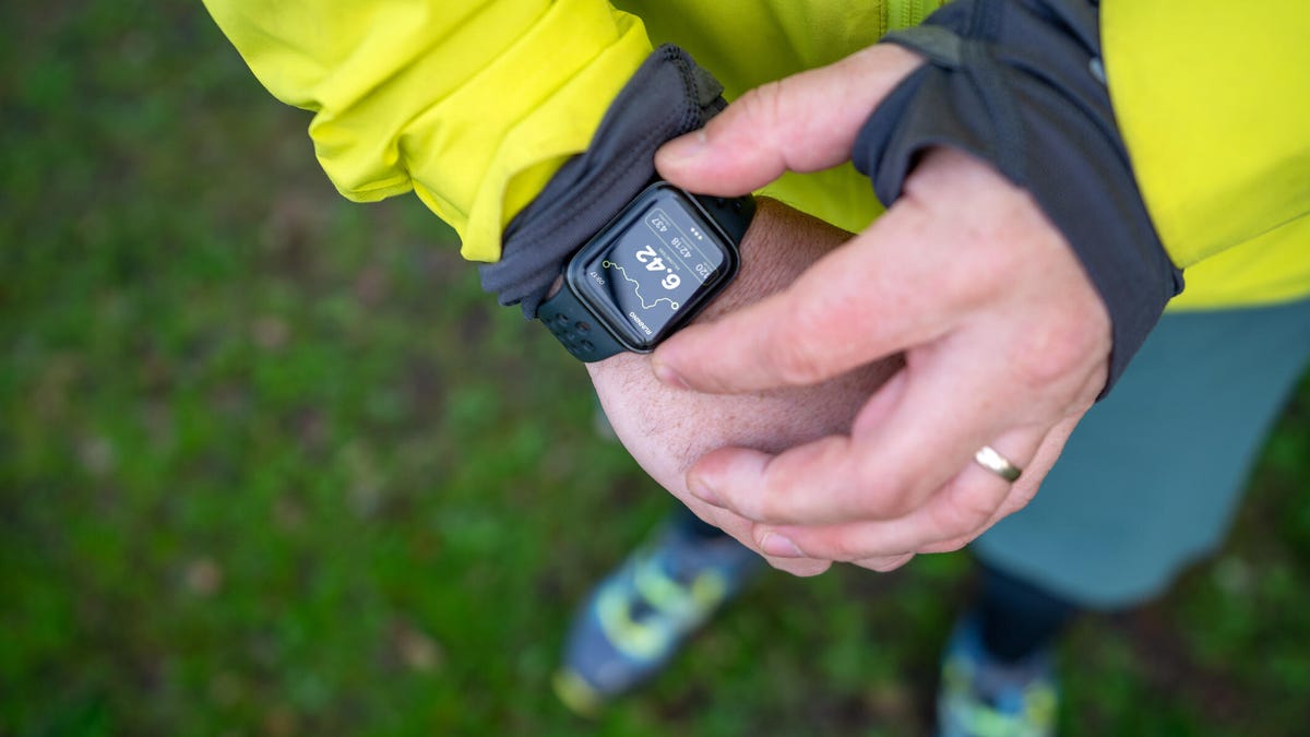 A man in yellow checks a fitness smartwatch on his wrist outside.