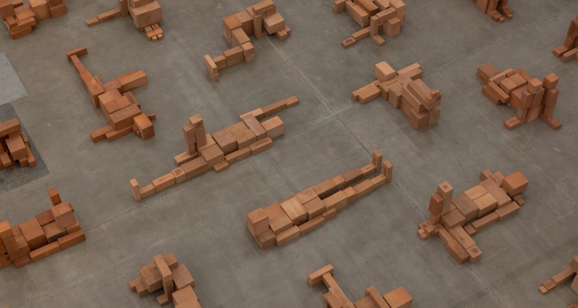 a detail of a room-size art installation by Antony Gormley of blocky terracotta forms resembling human figures in various positions