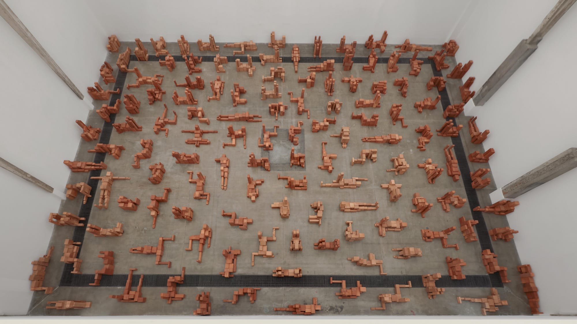 an aerial overview of a room-size art installation by Antony Gormley of blocky terracotta forms resembling human figures in various positions
