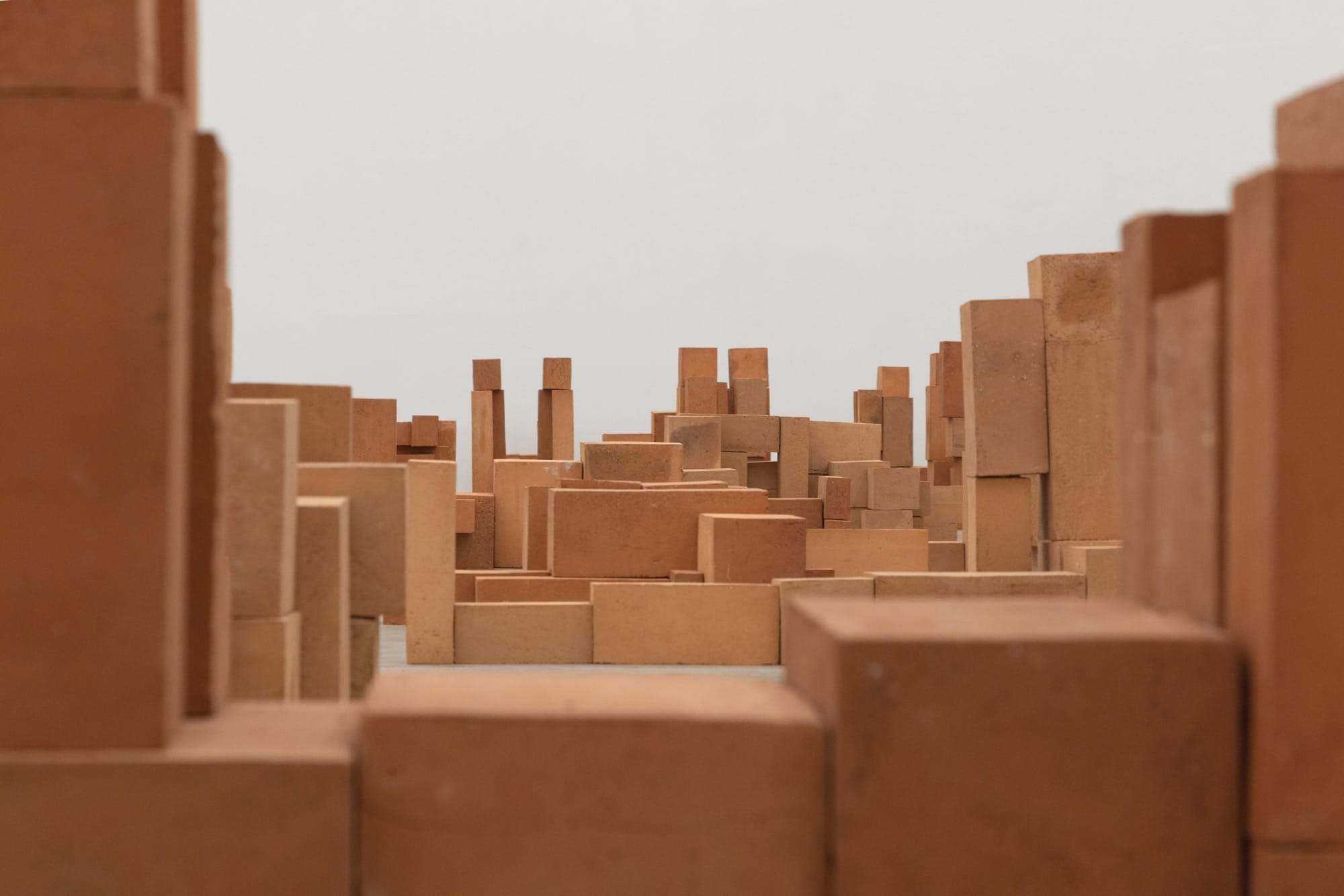 a detail of a room-size art installation by Antony Gormley of blocky terracotta forms resembling human figures in various positions