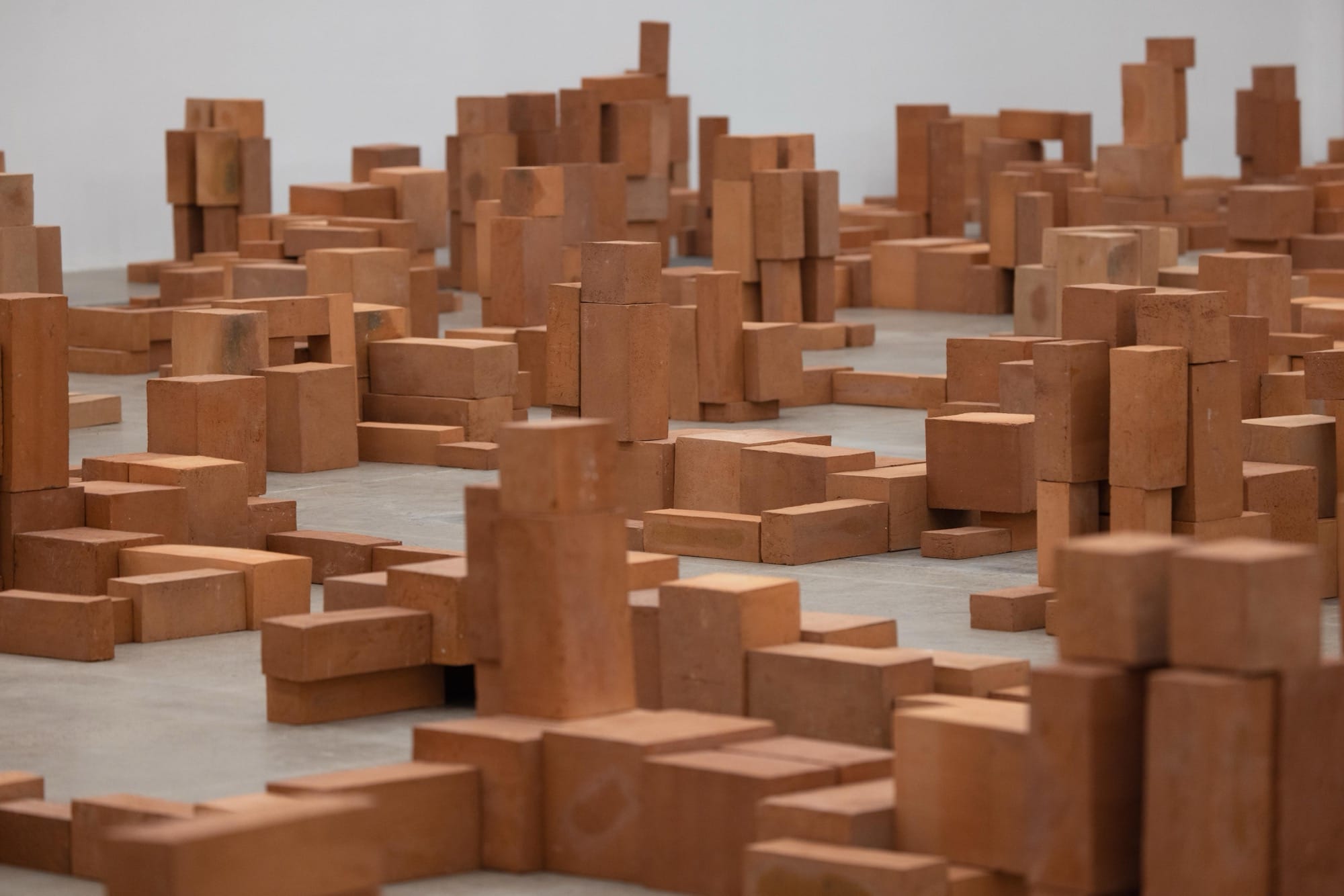 a detail of a room-size art installation by Antony Gormley of blocky terracotta forms resembling human figures in various positions