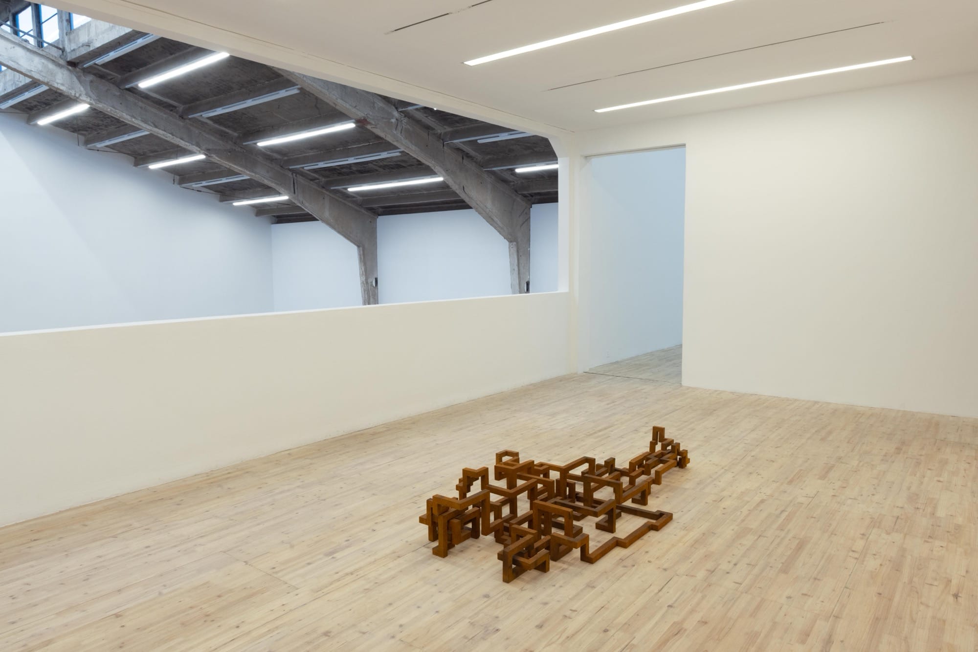 a sculpture by Antony Gormley installed in a white gallery space, depicting a blocky, abstract figure resembling a human lying prostrate on the floor