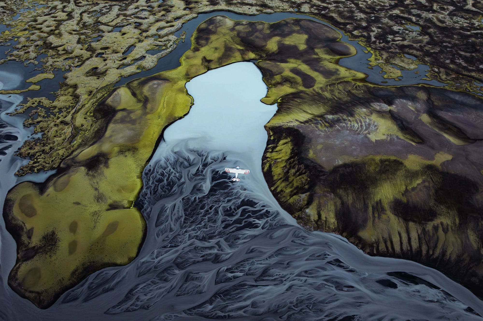a dramatic Iceland landscape photographed from the air by Dani Guindo showing rivers, a glacial lake, and a tiny plane