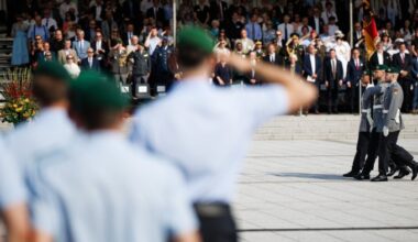 Soldiers in uniform carry a German flag during an oath-taking ceremony in Berlin as a crowd watches and salutes.