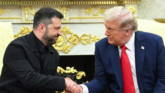 Volodymyr Zelenskyy and Donald Trump shake hands and look at each other during a meeting in the Oval Office.